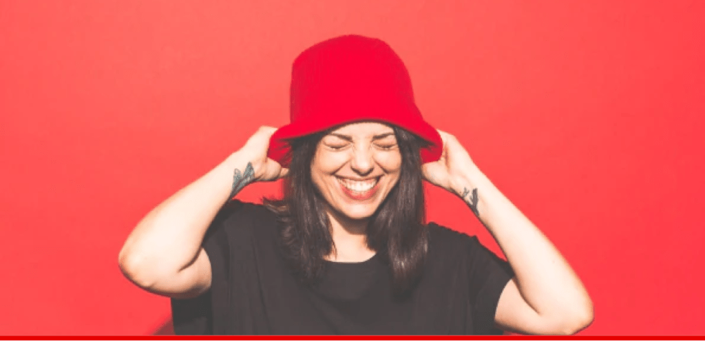 Woman in black t-shirt pulling down a red hat and smiling.