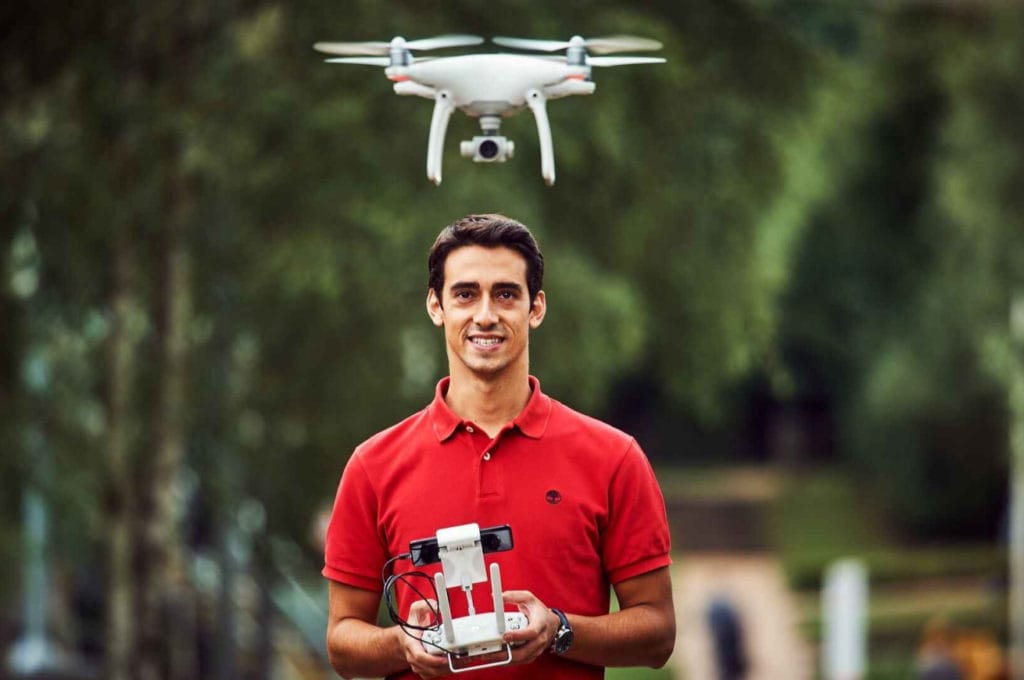 Man in a red shirt holding a drone controller with the drone above his head.