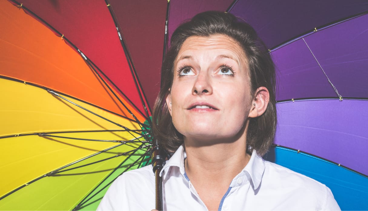 Lady holding a rainbow coloured umbrella, looking up to the sky.