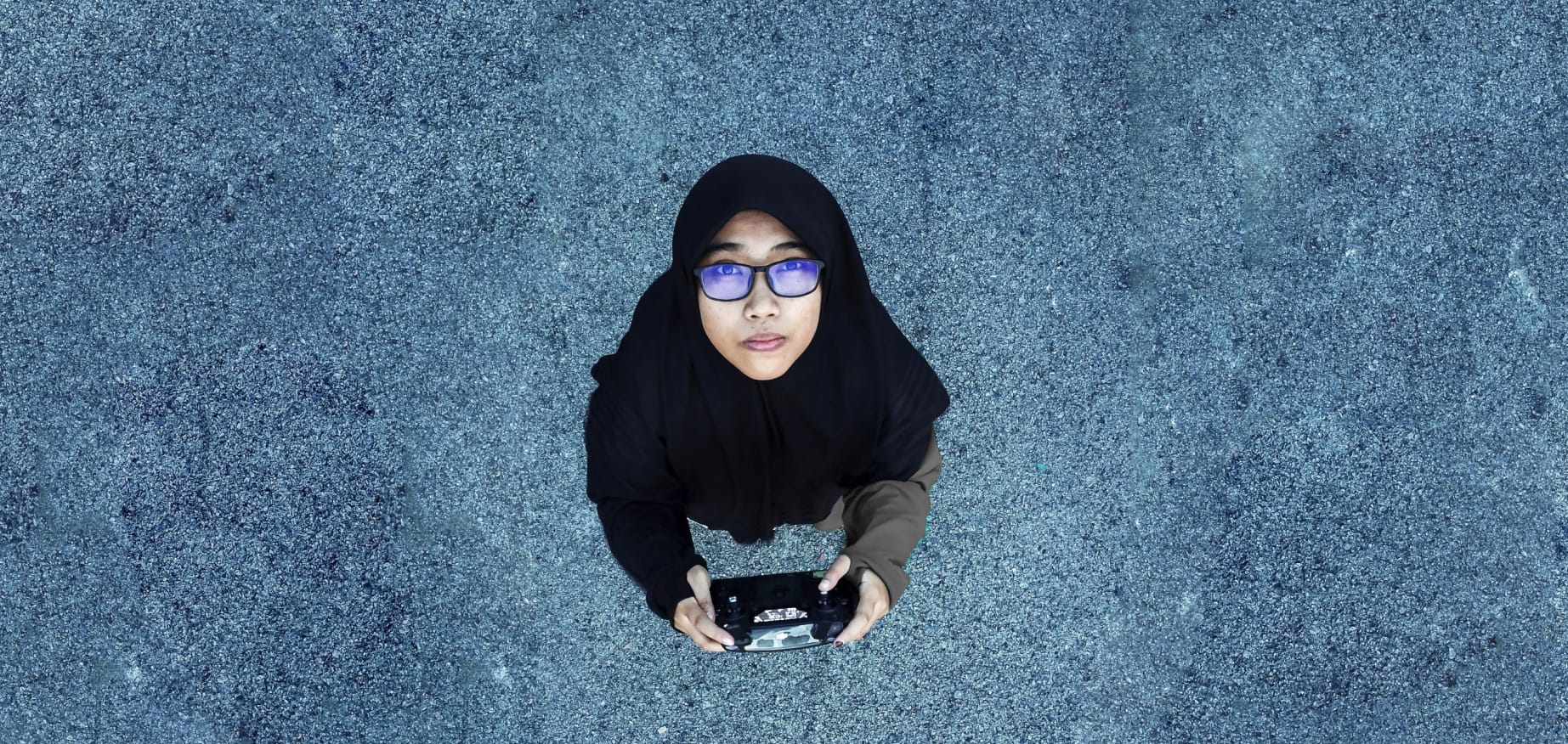 Woman looking up at the sky, holding a drone controller.