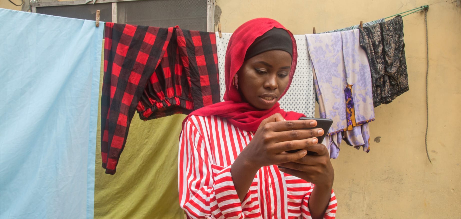 Young woman looking at her mobile phone, in front of a washing line.