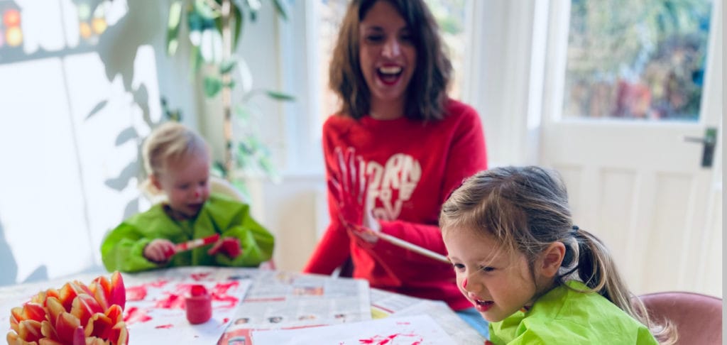 Woman laughing with two children, whilst they paint at the kitchen table.