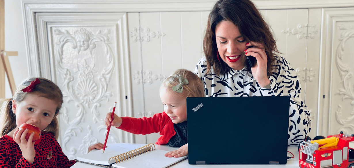 Woman talking on a phone, working on a laptop, surrounded by two children.