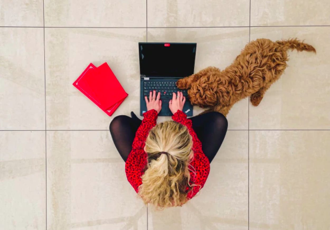 Woman sitting cross-legged on the floor with laptop and dog.