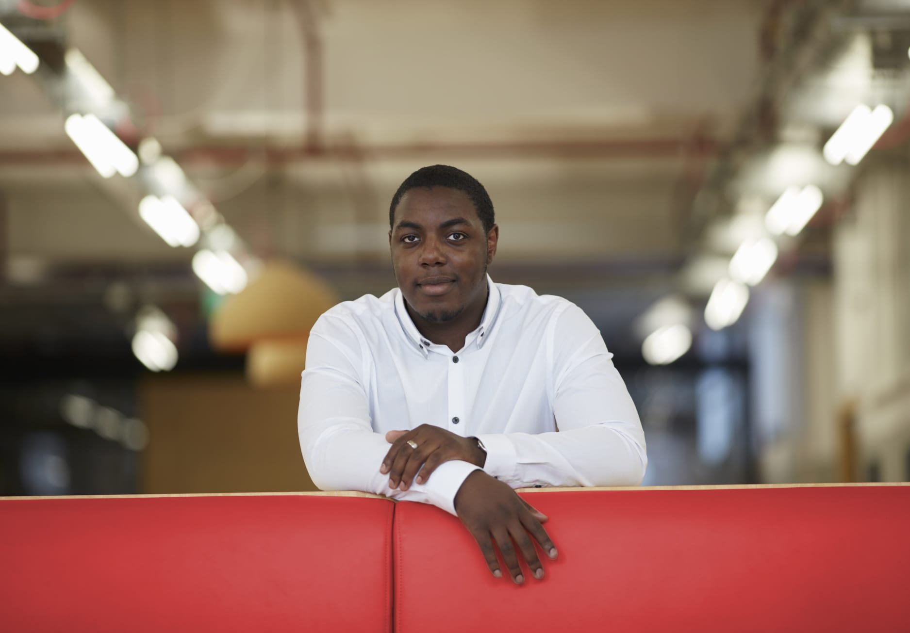 Man in a white shirt smiles while leaning on a red bench.