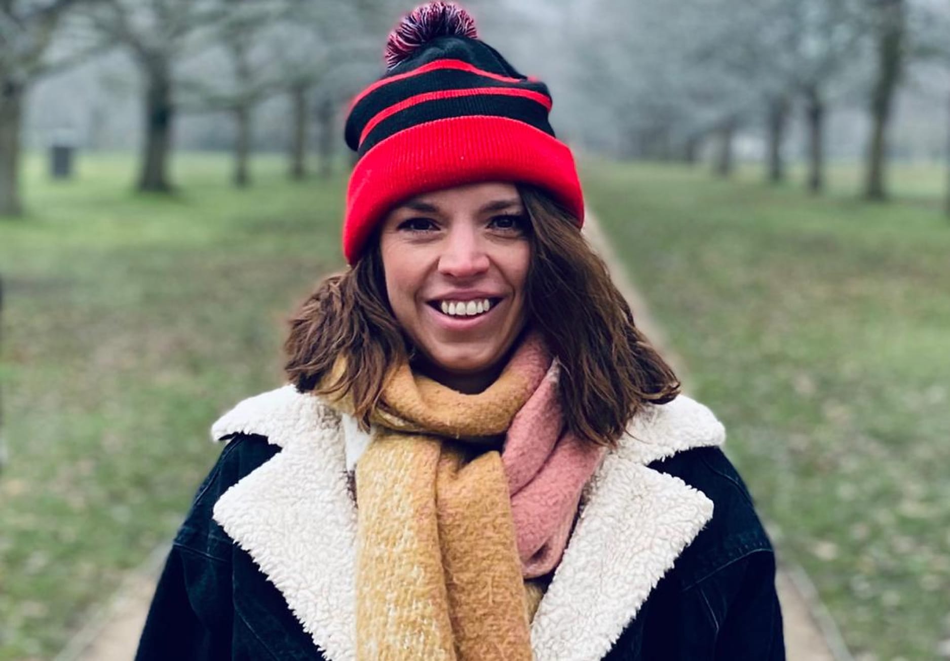 Woman wearing a red bobble hat and thick scarf, smiling.