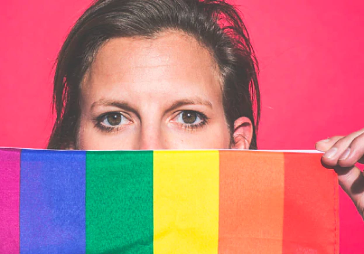 Woman looking out over a rainbow coloured fabric.