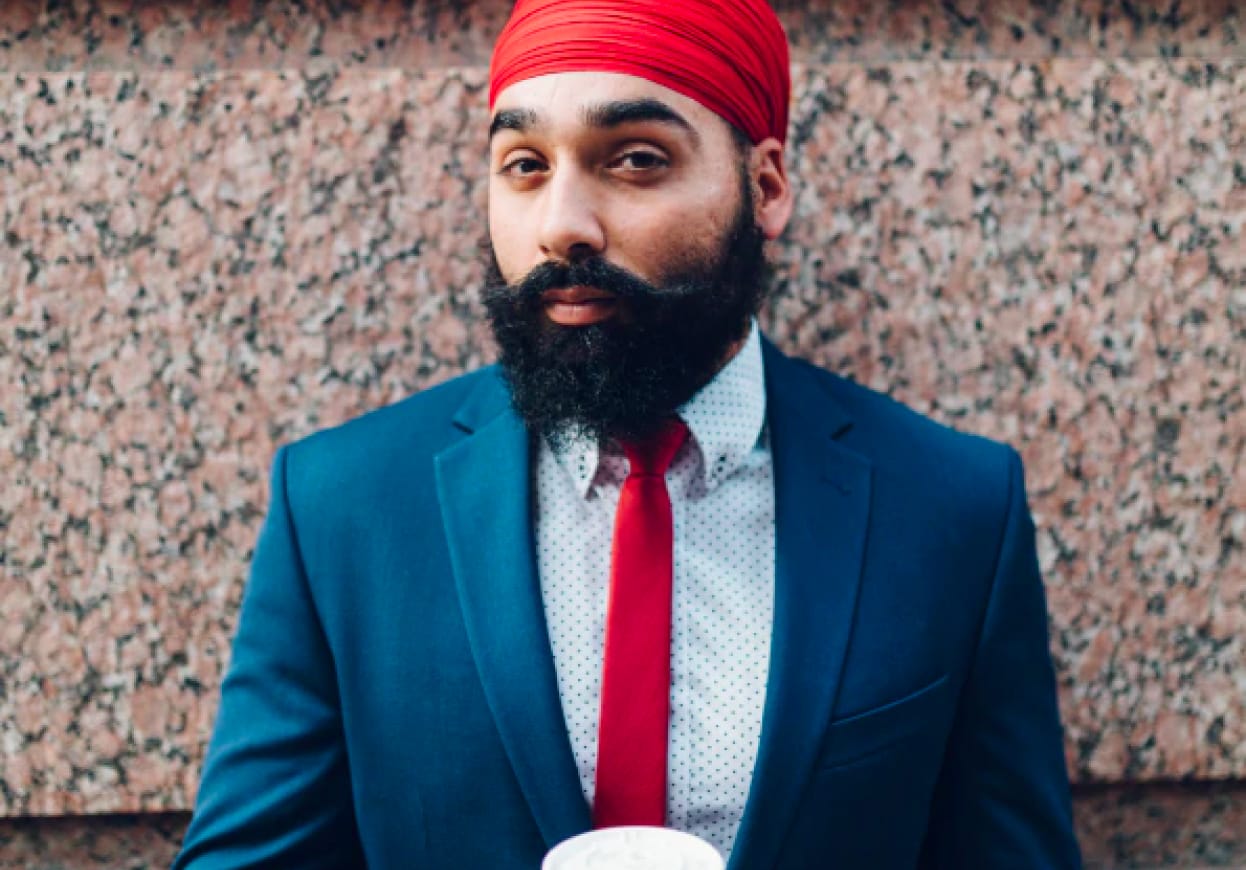 Man wearing a suit with a red tie and a beard, holding a cup of coffee.