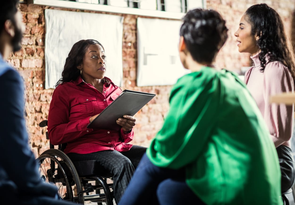 Woman in a wheelchair wearing a red shirt talking with two other women.