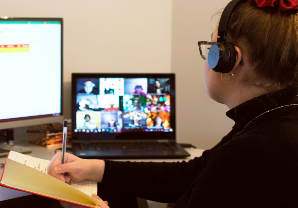 Woman wearing headphones, making notes whilst on a video call.