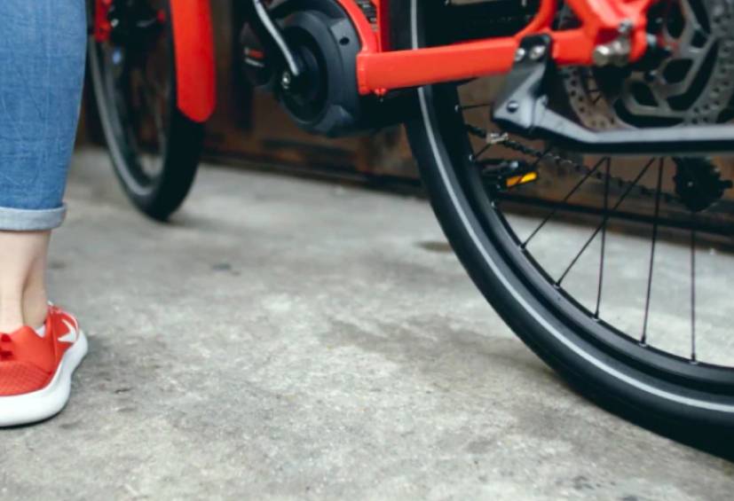 Leg in jeans and red trainer next to a red bike.